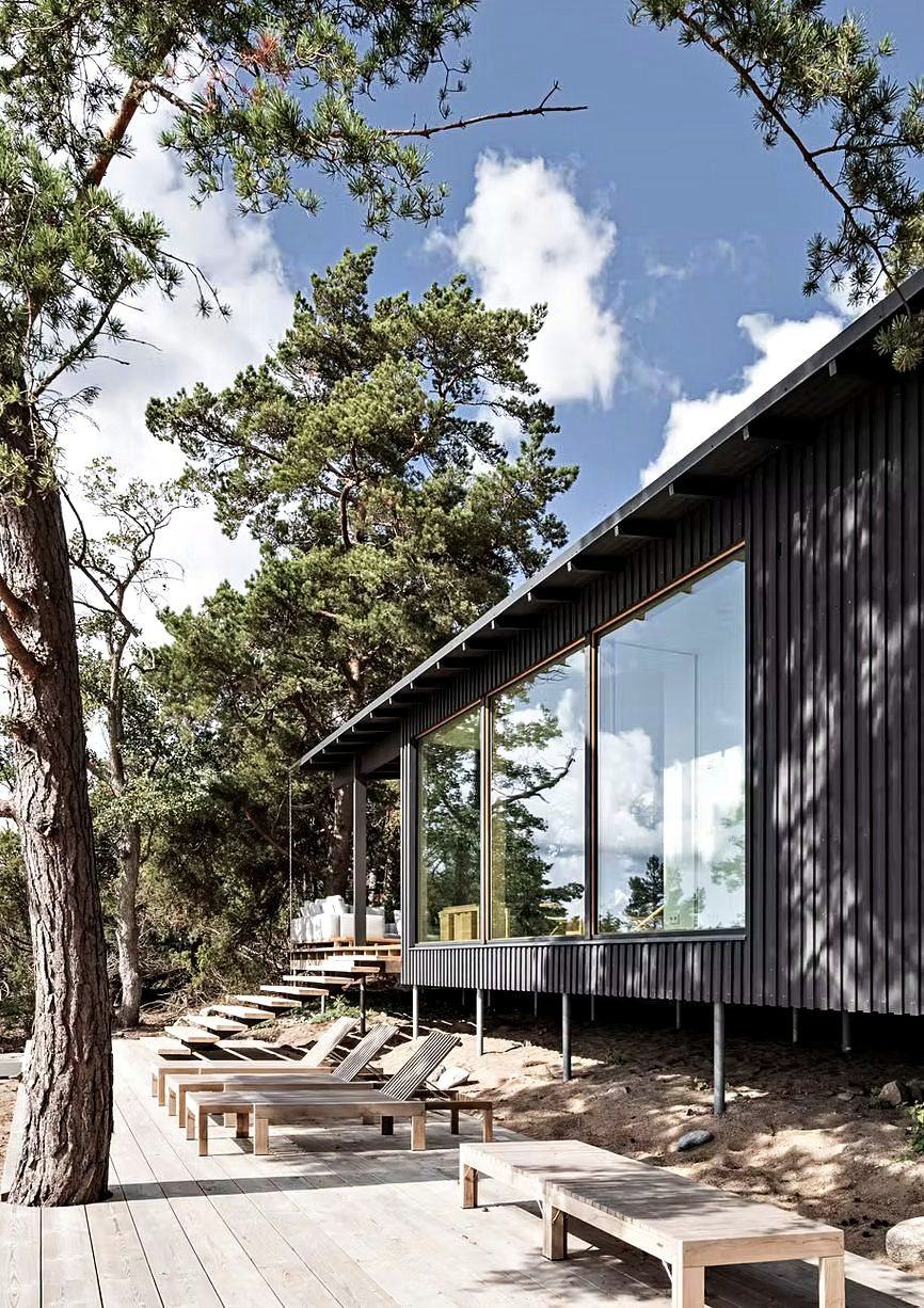 Black timber house with loungers on a deck beneath the pines