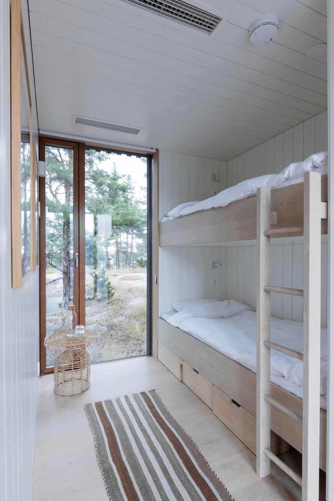 A bunk bed in pale oak beside a tall window onto the pines