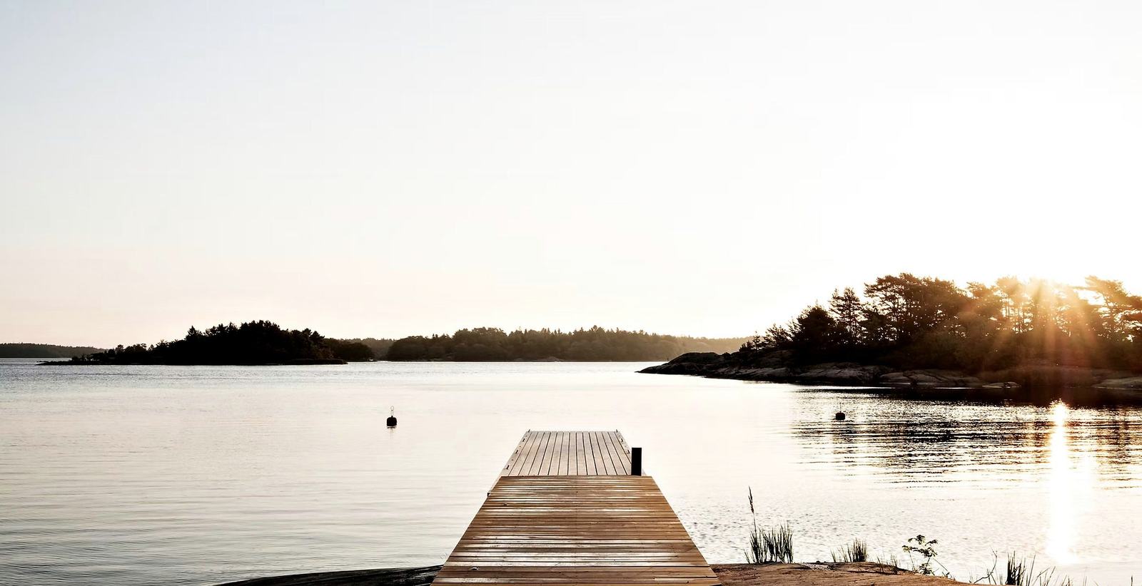 A timber pier reaching into calm water, wooded islands and low evening sun