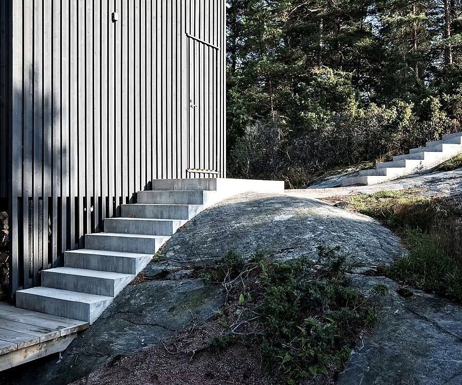 Concrete steps rising over granite beside a black timber building